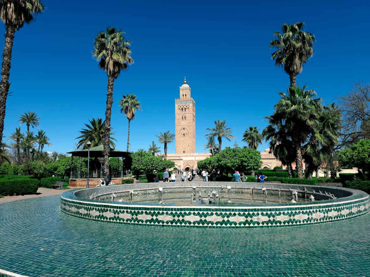 Koutoubia minaret beyond a walled garden pool and palms in Marrakech